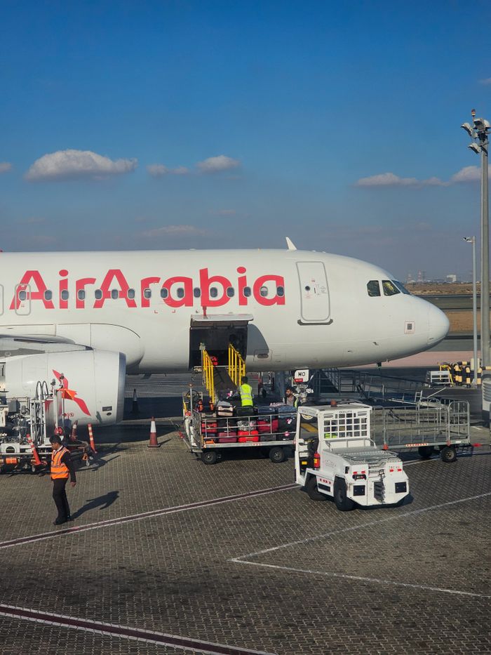 Air Arabia Airbus A320 being loaded at a sunny airport tarmac.