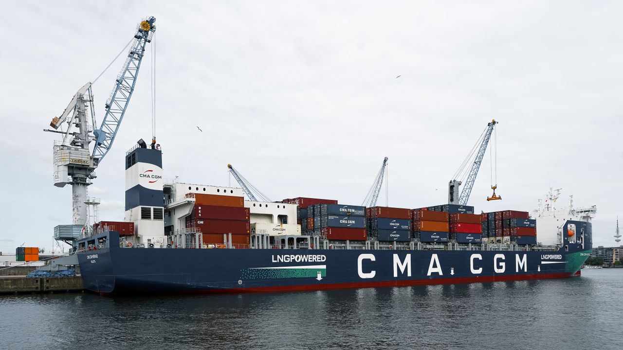 A large container ship docked at Hamburg port with cranes and containers visible, showcasing global trade.